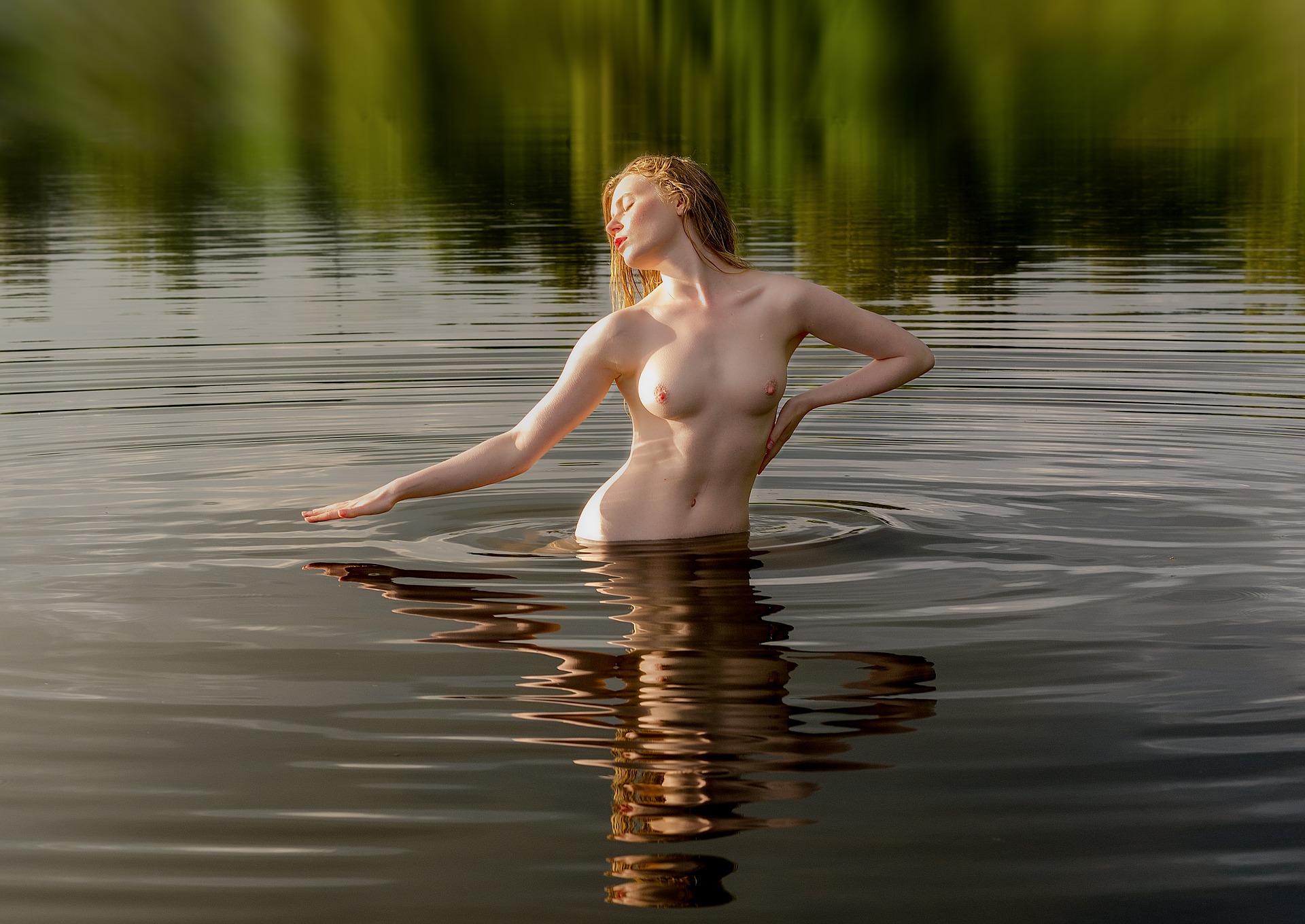 Загорелая голая девушка купается в реке